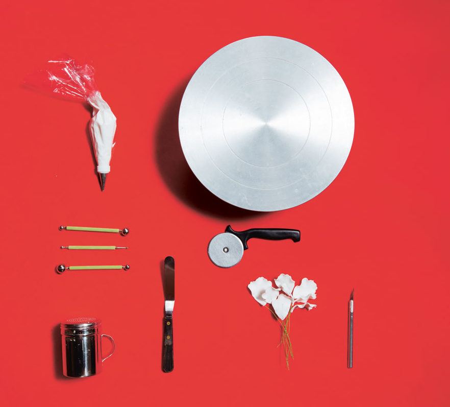Among the many essentials in Penk Ching's kit are (clockwise from top left) a piping bag with royal icing and small round metal tip, cake turner, scalpel. orchid made of gum paste, small dough wheel cutter, off set metal spatula, confectioner's sugar strainer. metal flower plunger, and modeling tools