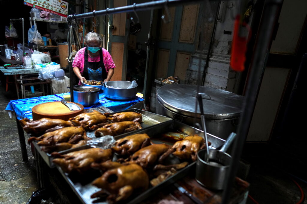 Janya Saetang, 55, a sister of Ladda Saetang who died at age 66 of the coronavirus disease in May works next to pans of stewed ducks at her late sister's food stall in Bangkok
