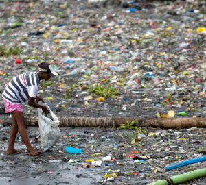 woman picks up plastic cups along the riverbank of Pasig river, in Manila, Philippines, which is one of the largest contributors to single-use plastics waste