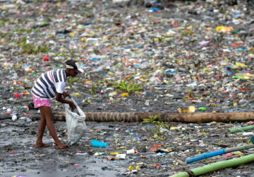 woman picks up plastic cups along the riverbank of Pasig river, in Manila, Philippines, which is one of the largest contributors to single-use plastics waste