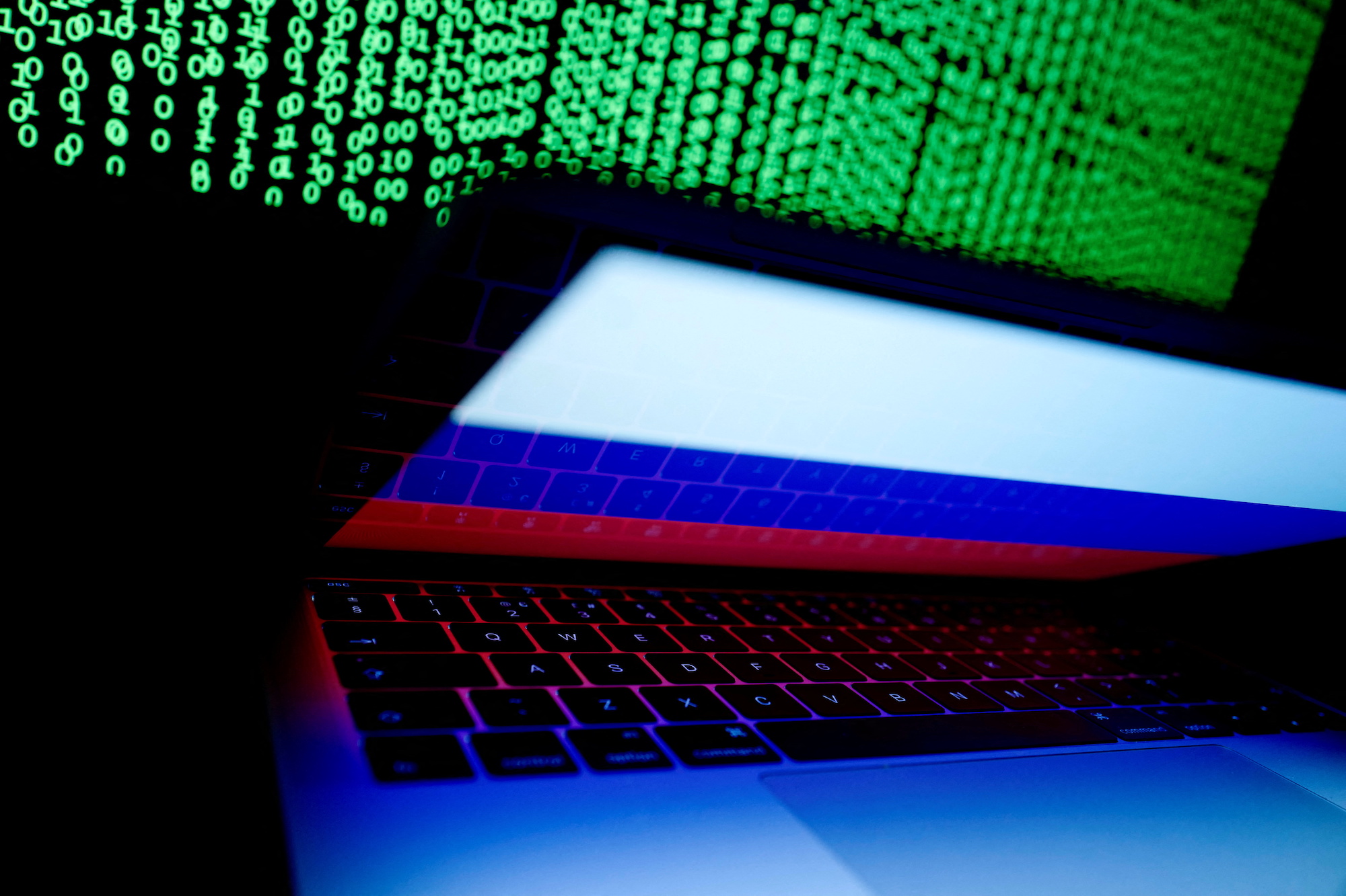A Russian flag is seen on the laptop screen in front of a computer screen on which cyber code is displayed, in this illustration picture taken March 2, 2018