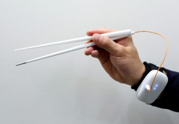 An employee of Kirin Holdings demonstrates chopsticks that can enhance food taste using an electrical stimulation waveform that was jointly developed by the company and Meiji University's School of Science and Technology Professor Homei Miyashita
