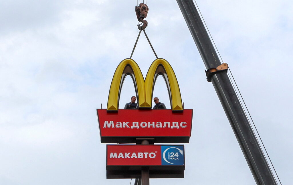 Workers use a crane to dismantle the McDonald's Golden Arches while removing the logo signage from a drive-through restaurant of McDonald's