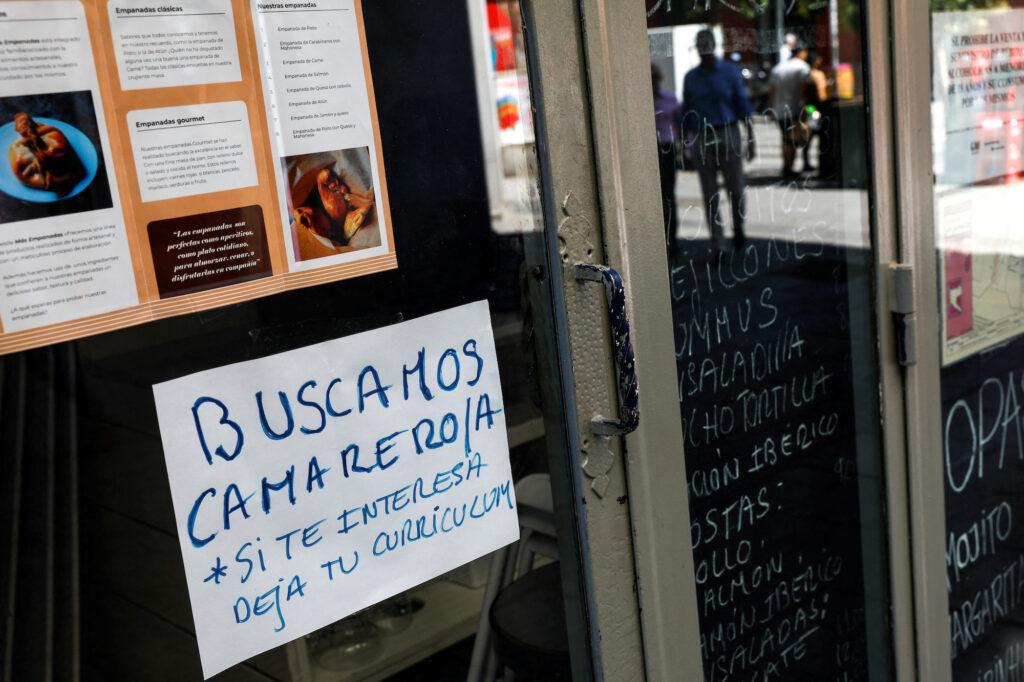 A sign that reads "Waiter needed. If interested, drop CV" is posted on the window of a restaurant in central Madrid, Spain