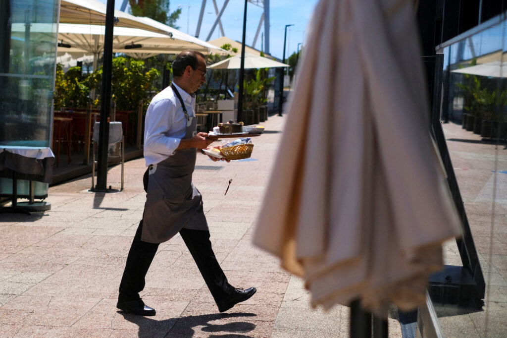No experience, no resume, you're hired! European hotels fight for staff:A waiter clears the table in a restaurant in Lisbon, Portugal