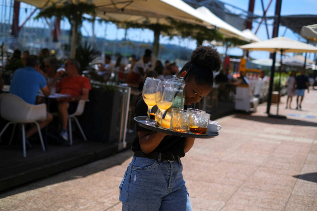 No experience, no resume, you're hired! European hotels fight for staff: A waitress removes drinks from a table in a restaurant in Lisbon, Portugal