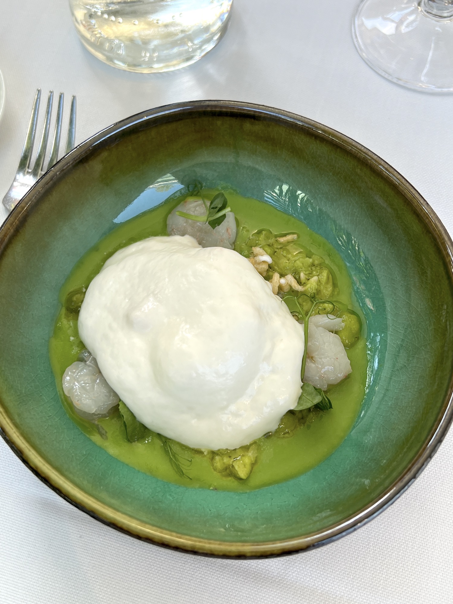A delicately poached egg topped with burrata cheese cream over a pea puree and shrimp