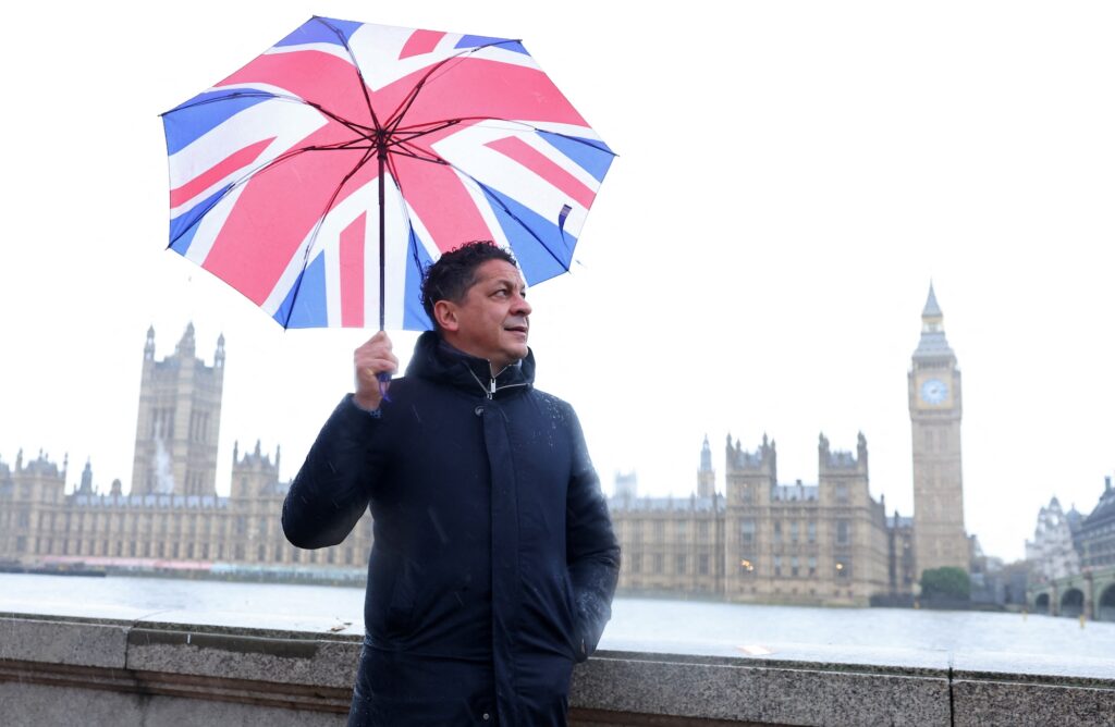 Italian chef-turned restaurant owner Francesco Mazzei shields from the rain as he poses for a portrait near the Houses of Parliament in London, Britain, November 14, 2023. REUTERS/Toby Melville